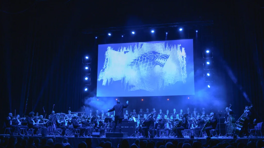 Teaserbild zu Game Of Thrones & House Of The Dragon mit Orchester und Projektion eines Wolfssymbols.