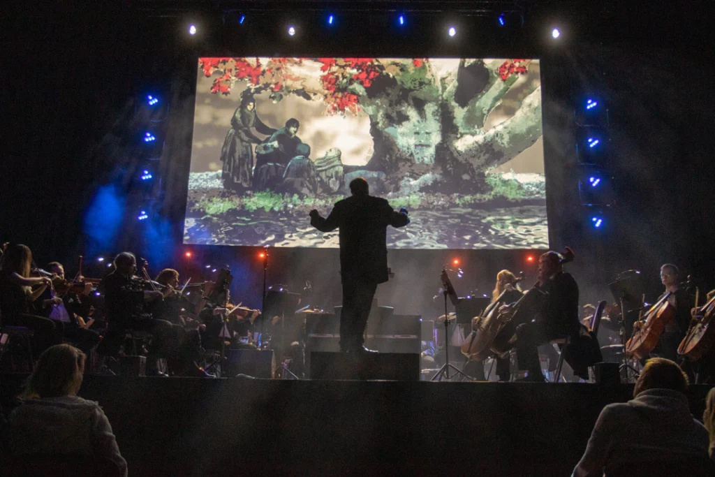 Teaserbild zu Game Of Thrones & House Of The Dragon mit Orchesteraufführung vor großem Bildschirm.