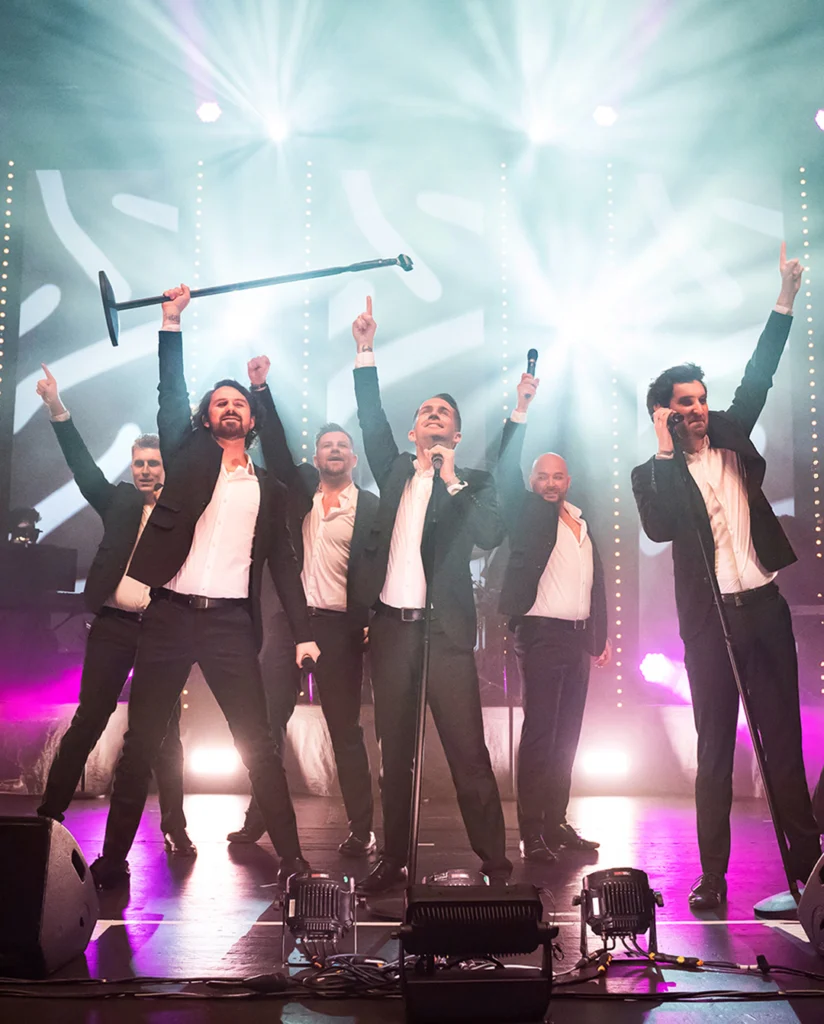 Teaserbild zu The 12 Tenors mit sechs Sängern auf der Bühne in Anzügen.
