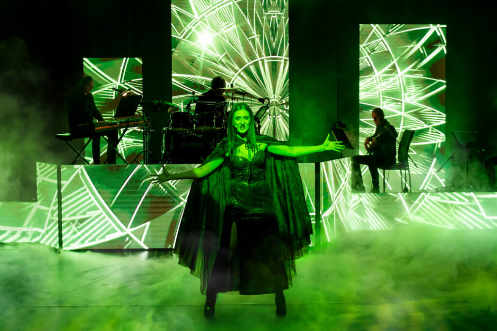Teaserbild zu Wicked mit einer Sängerin auf der Bühne vor grünen Lichteffekten.