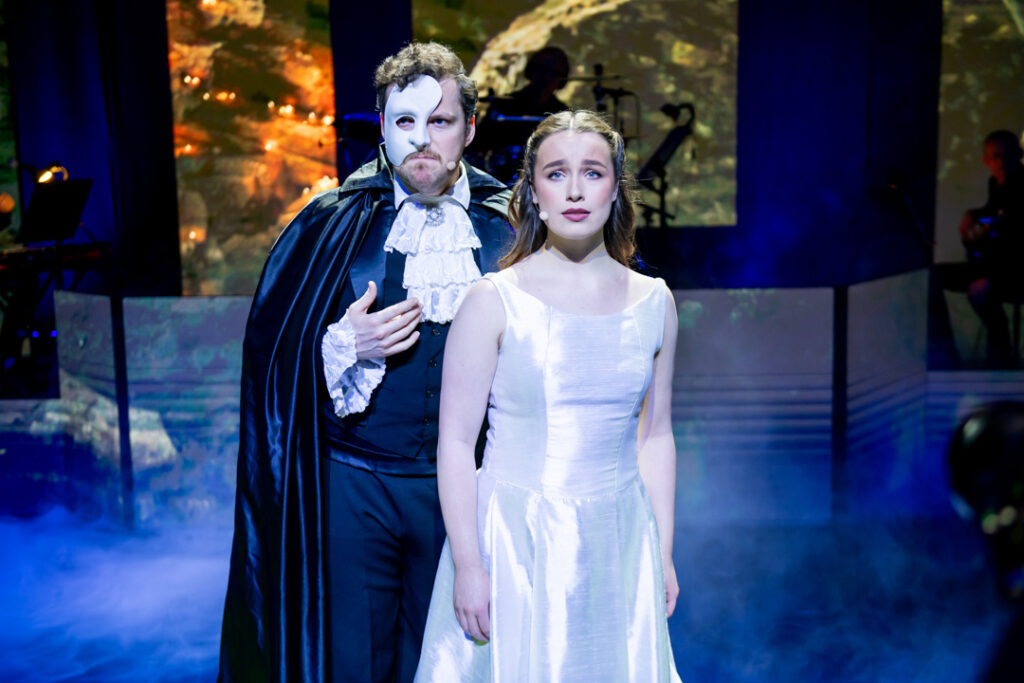 Szenenbild aus Das Phantom der Oper mit einem Mann in Maske und einer Frau in einem weißen Kleid.