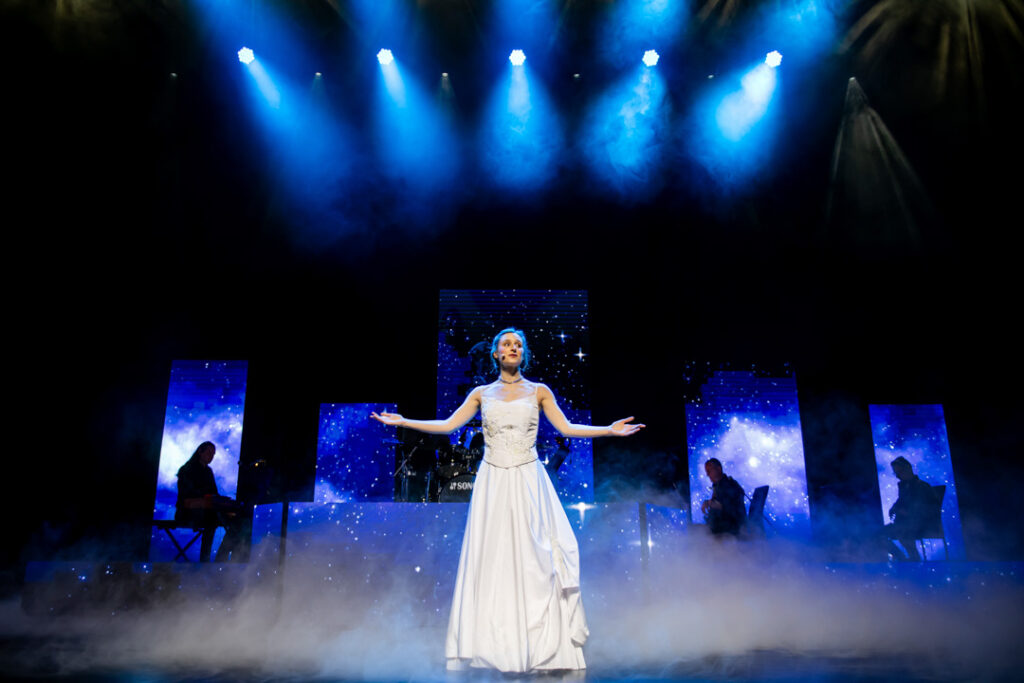 Teaserbild zu Evita mit einer Sängerin in einem weißen Kleid auf der Bühne.