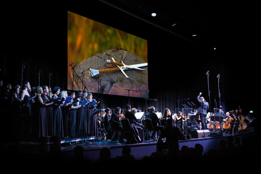 Teaserbild zu Der Herr der Ringe mit einem Orchester und einer Chorgemeinschaft auf der Bühne.