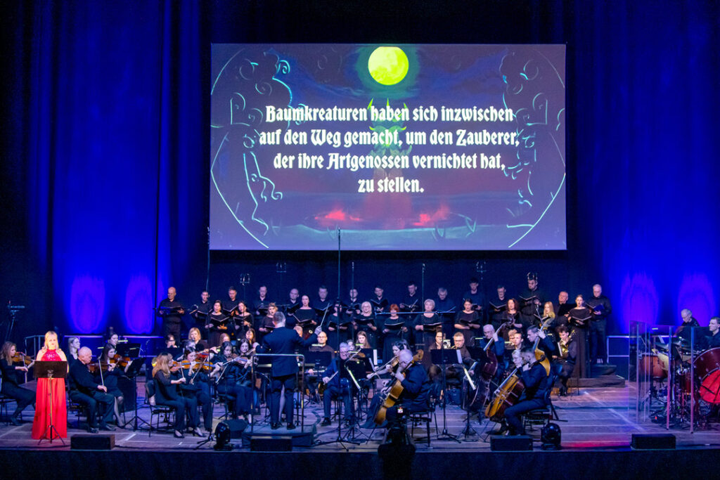 Teaserbild zu Der Herr der Ringe mit einem Orchester und einem großen Bildschirm im Hintergrund.