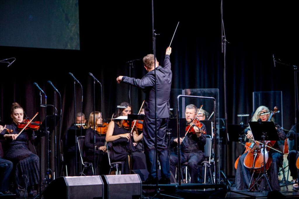Orchesteraufführung mit Dirigent und Musikern auf der Bühne.