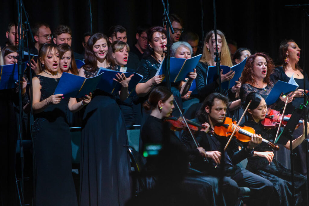 Choraufführung mit Sängern in schwarzen Kleidern und Musikern mit Instrumenten.