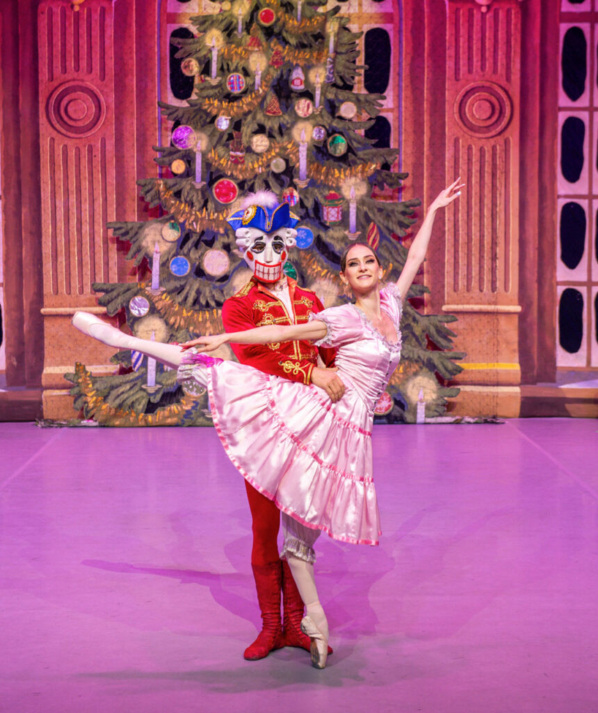 Tanzende Balletttänzer in Kostümen vor einem festlich geschmückten Weihnachtsbaum.