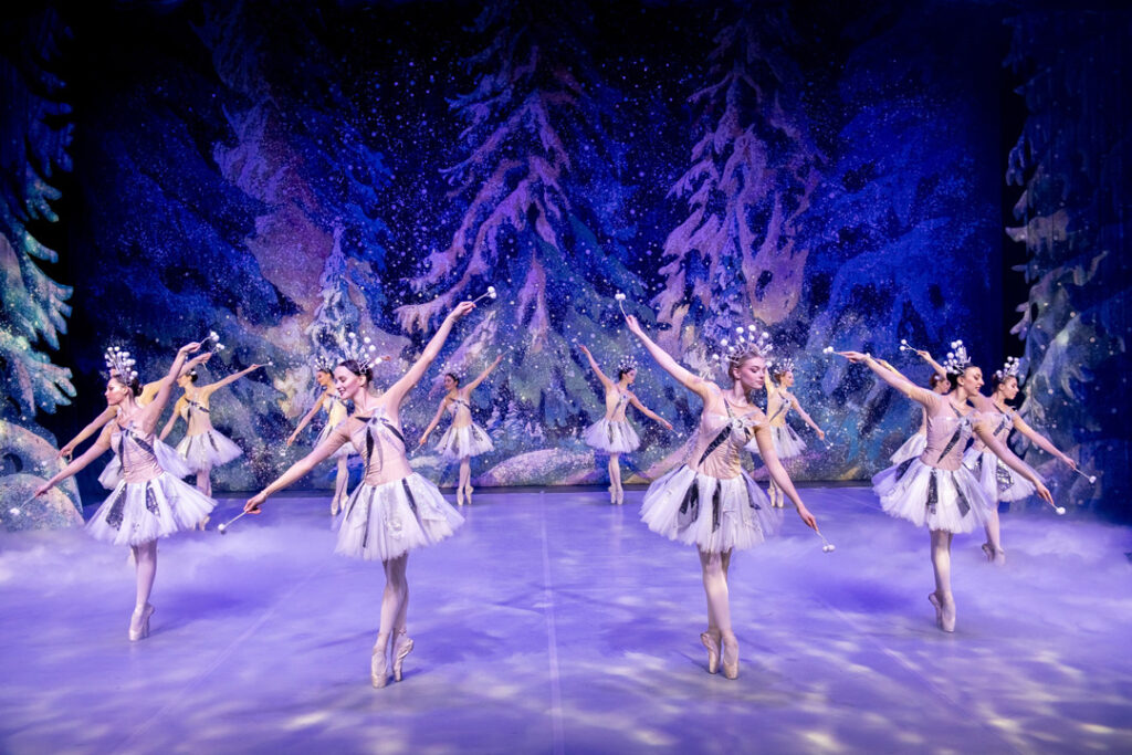 Tanzende Ballerinas in weißen Kostümen auf einer Bühne mit winterlicher Kulisse.