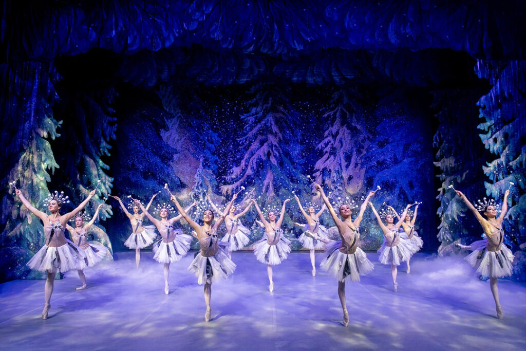 Tanzende Balletttänzerinnen in weißen Kostümen auf einer Bühne mit winterlicher Kulisse.