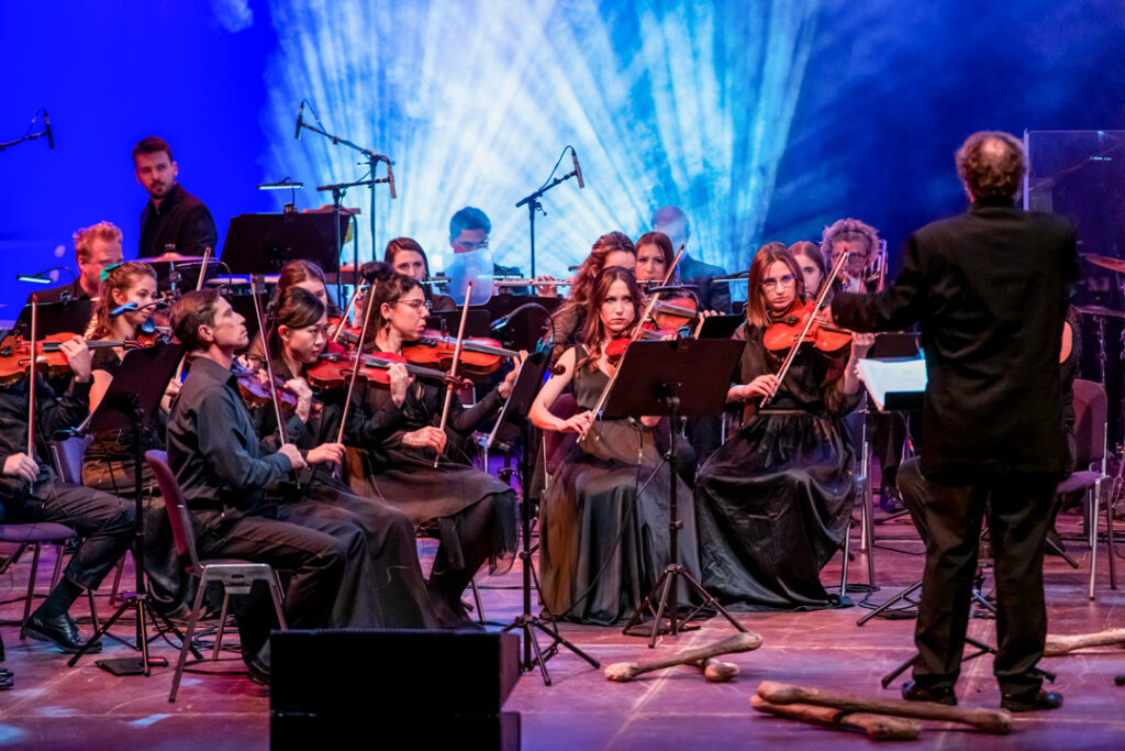 Orchesteraufführung mit Musikern in schwarzer Kleidung, die Violinen spielen.