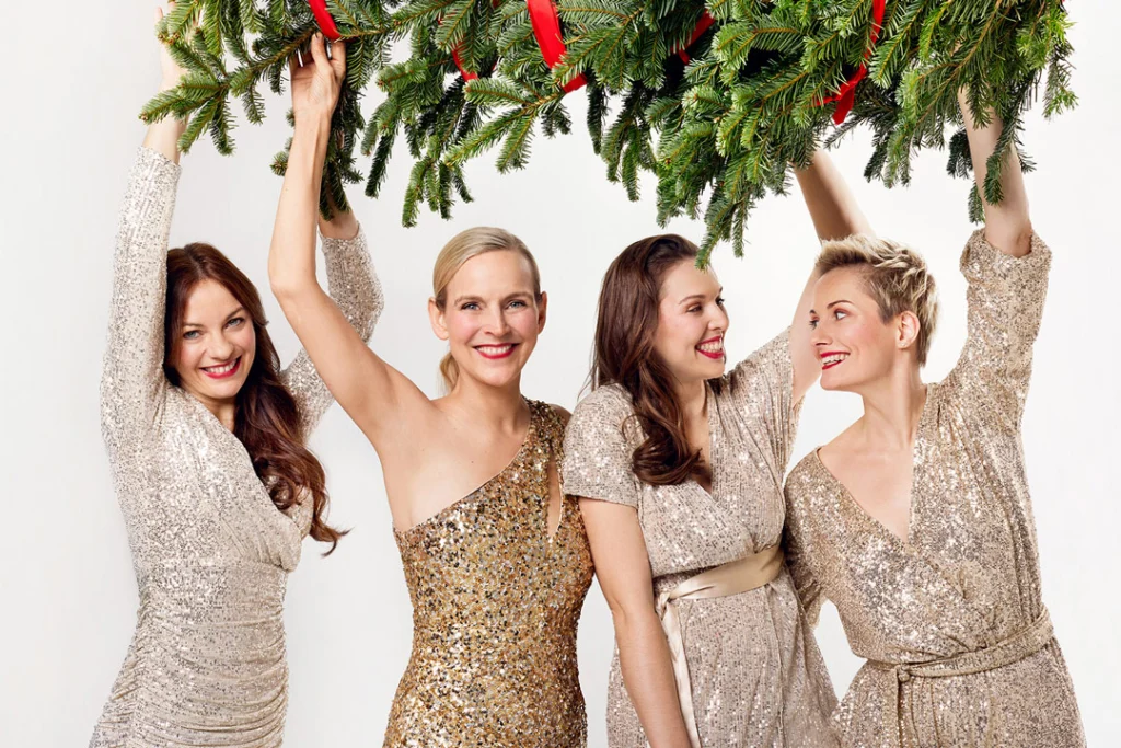 Teaserbild zu Weihnachten mit Salut Salon, vier Frauen in glitzernden Kleidern mit Tannenzweigen.