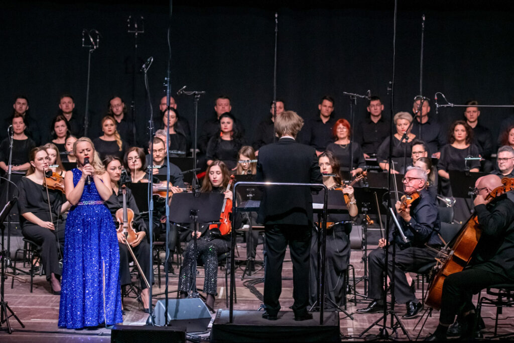 Auftritt mit Sängerin in blauer Robe vor einem Orchester während eines Konzerts.