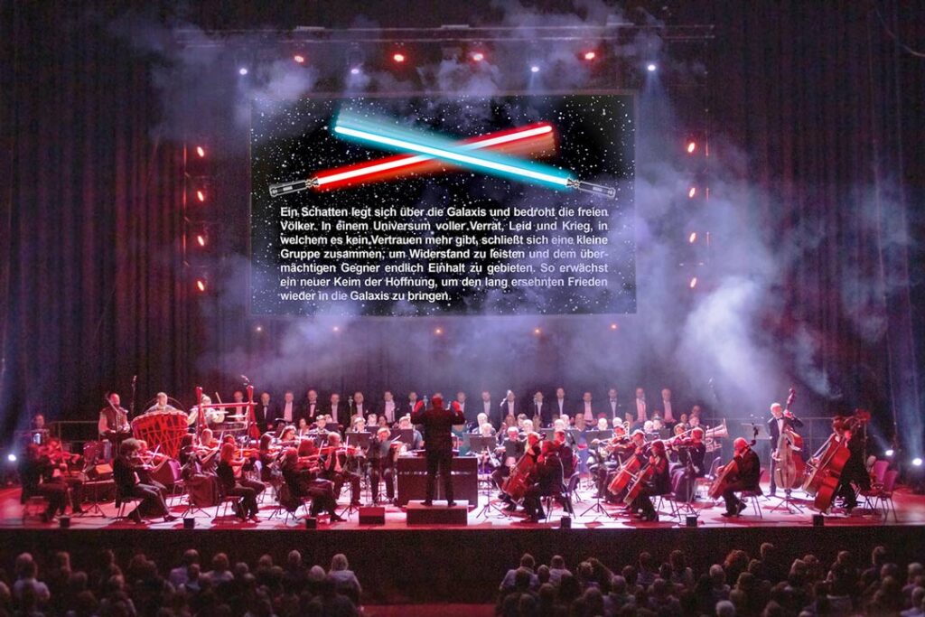 Teaserbild zu The Music of Star Wars mit Orchester und Lichtschwertern im Hintergrund.