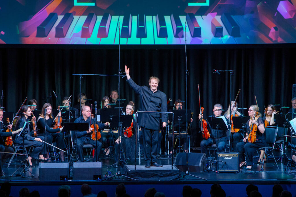 Teaserbild zu The Magic of Hans Zimmer mit einem Orchester und einem Dirigenten auf der Bühne.