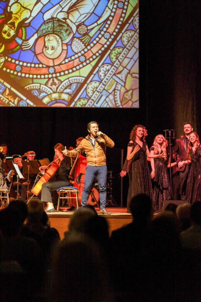 Teaserbild zu Highlights der schönsten Musicals mit einem Sänger auf der Bühne und einem Orchester im Hintergrund.