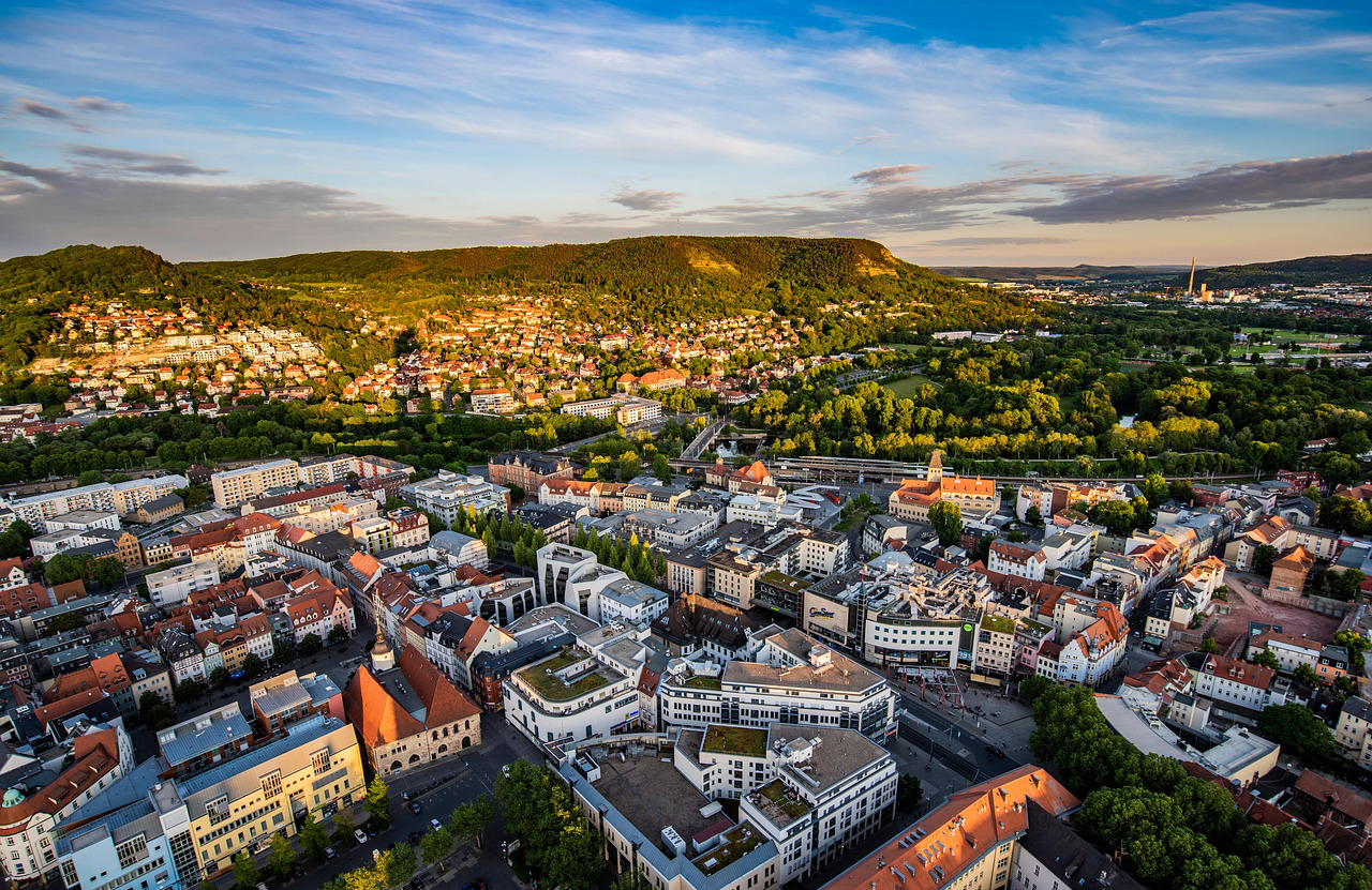 Luftaufnahme der Stadt Jena mit grünen Hügeln im Hintergrund.