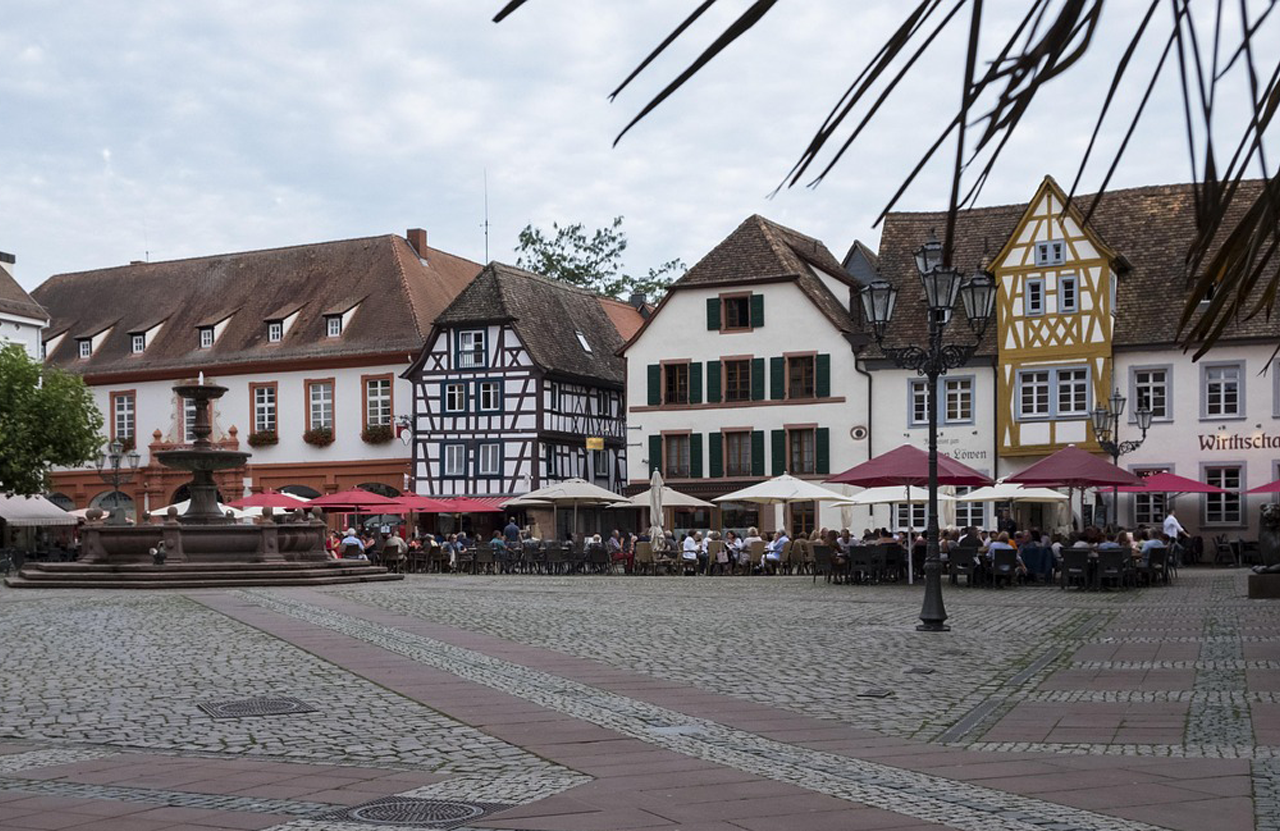 Stadtansicht von Neustadt an der Weinstraße mit historischen Gebäuden und einem Platz voller Gäste.