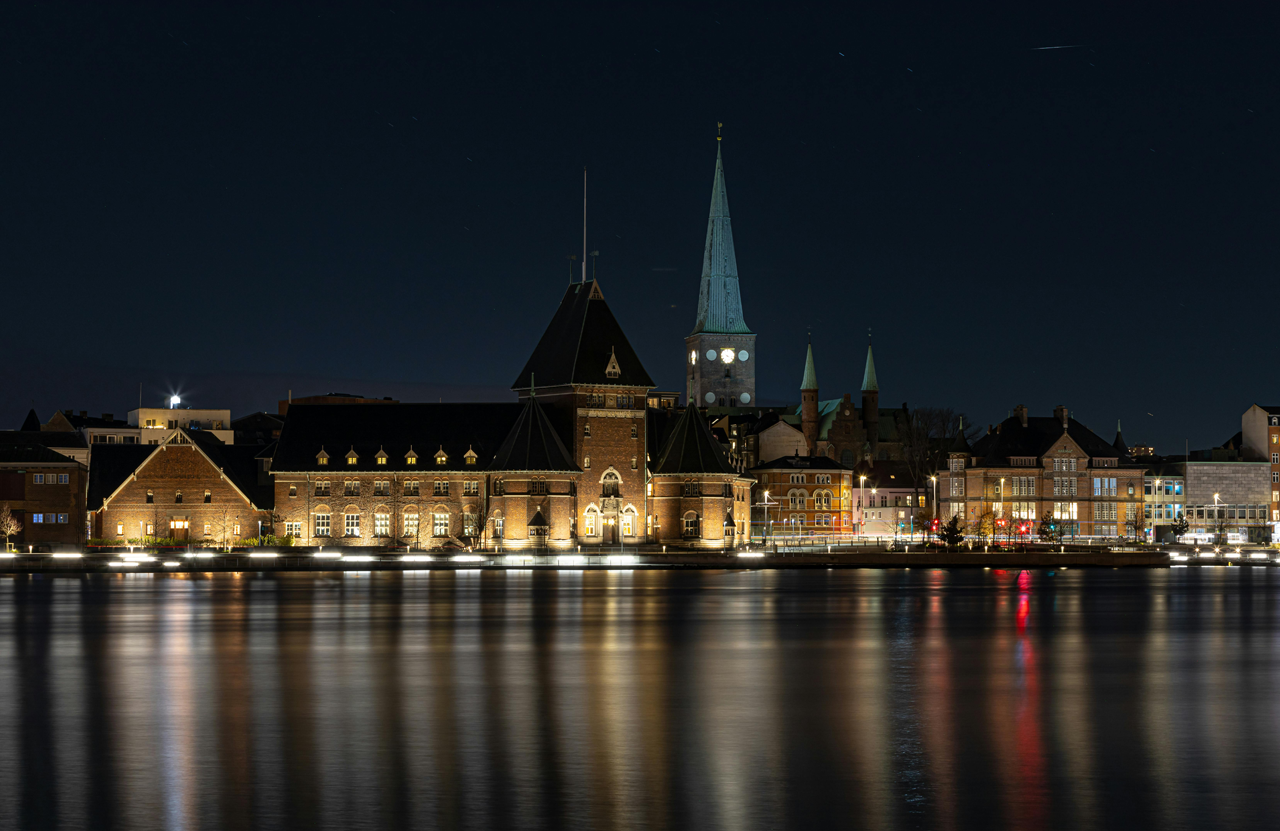 Nachtansicht der Stadt Aarhus mit beleuchteten Gebäuden und reflektierendem Wasser.