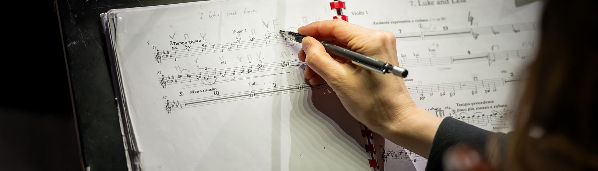 Hand, die Noten auf einem Musikblatt mit Bleistift bearbeitet.