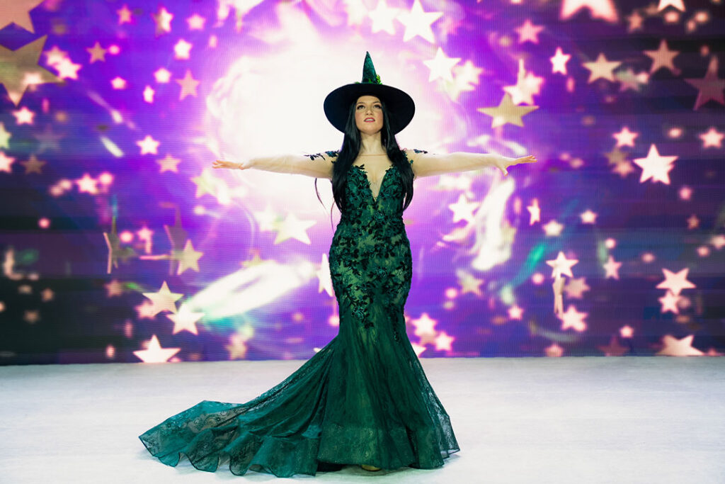 Teaserbild zu Musical Dreams mit einer Sängerin in einem grünen Kleid und Hexenhut vor einem funkelnden Hintergrund.