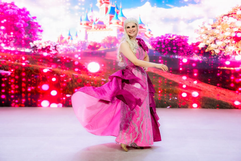 Teaserbild zu Musical Dreams mit einer Tänzerin in pinkem Kleid vor einer bunten Märchenlandschaft.