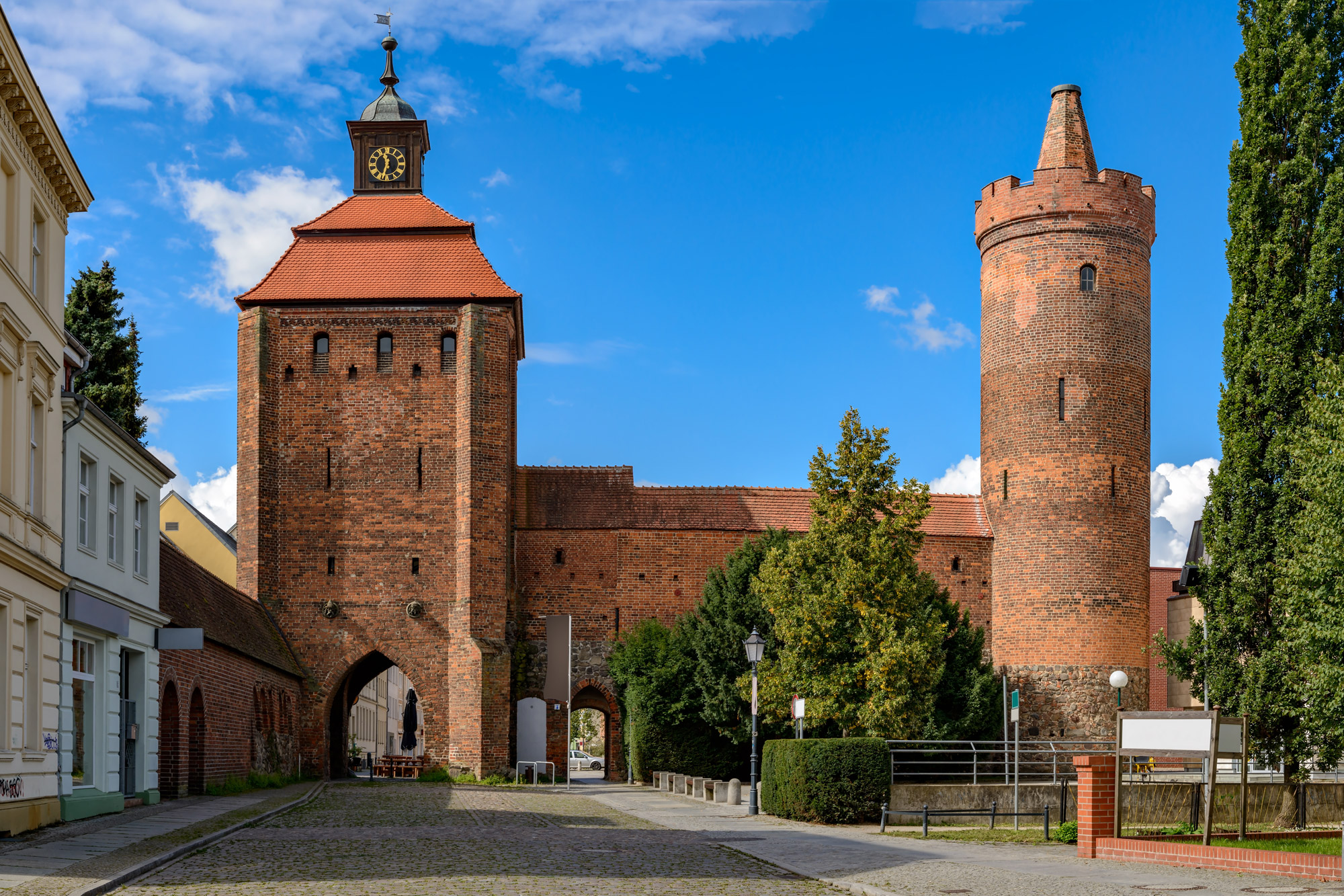 Stadtmauer von Bernau mit Uhrturm und Rundturm unter blauem Himmel.